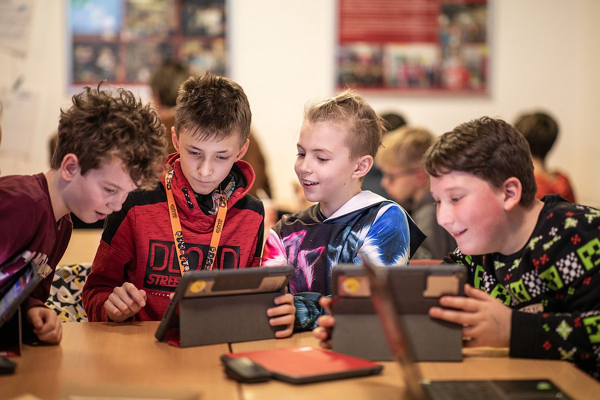 Foto von vier Kindern mit fröhlichem Ausdruck, die gemeinsam auf Laptops schauen